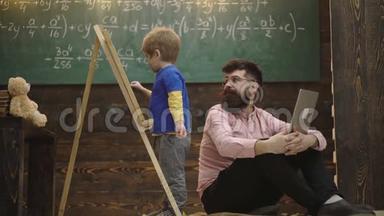 男孩在黑板上用粉笔写字. 可爱的蹒跚学步的男孩在木制背景上画黑板。 人控制学习